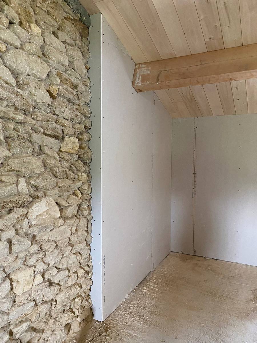 Doublage isolant en plaques de plâtre contre un mur en pierre, sous plafond bois – Cabesos & Fils